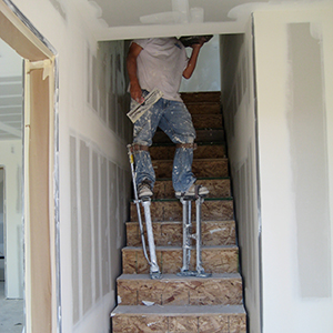 A man using plastering stilts on stairs